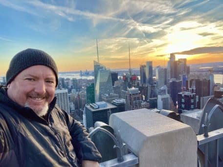 a selfie of Kevin in front of a city skyline on a road trip for MMM